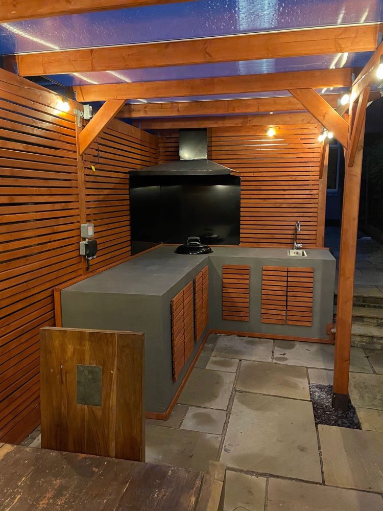 An example of a pergola with a kitchen area under it with seating at night.