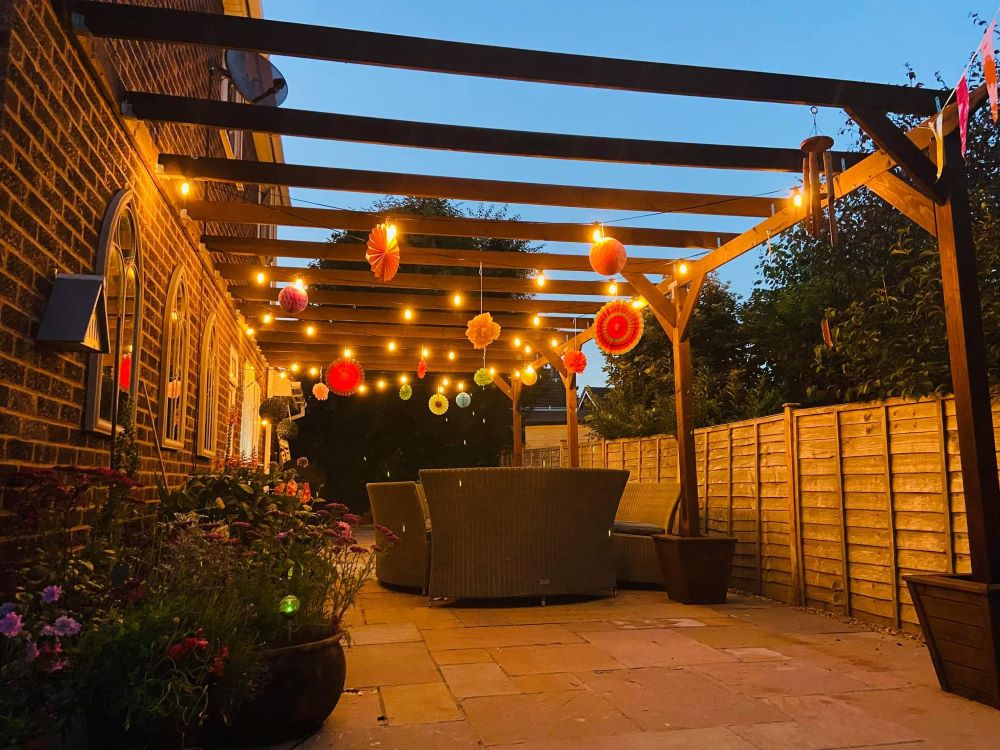 An example of a pergola, in the evening with lanterns and lights with a dining table underneath it.